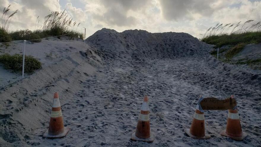 Sand dune rising up, footsteps in them, cones in front of the pathway blcoking off the entrance to the beach