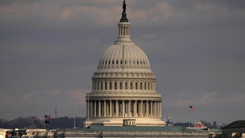 The United States Capitol building in Washington, D.C., with its dome and the Statue of Freedom perched on top. The sky in the background is filled with dark clouds.