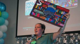 Kim McMilin holds aloft an enlarged prop version of one of three new limited edition library card designs unveiled Tuesday, Sept. 1, 2026 at the Soldotna Public Library in Soldotna, Alaska.