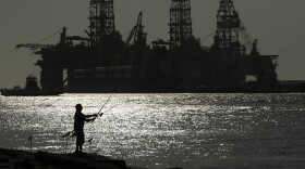 A man wears a face mark as he fishes near docked oil drilling platforms. (Eric Gay/AP)