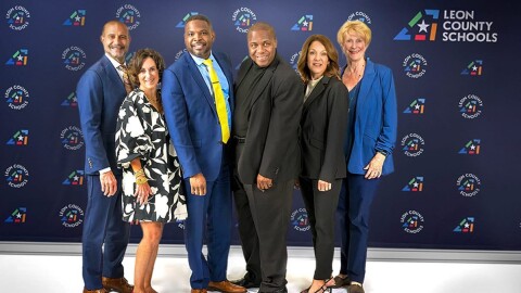 Leon County school board members pose and smile in front of a backdrop with the school district logo