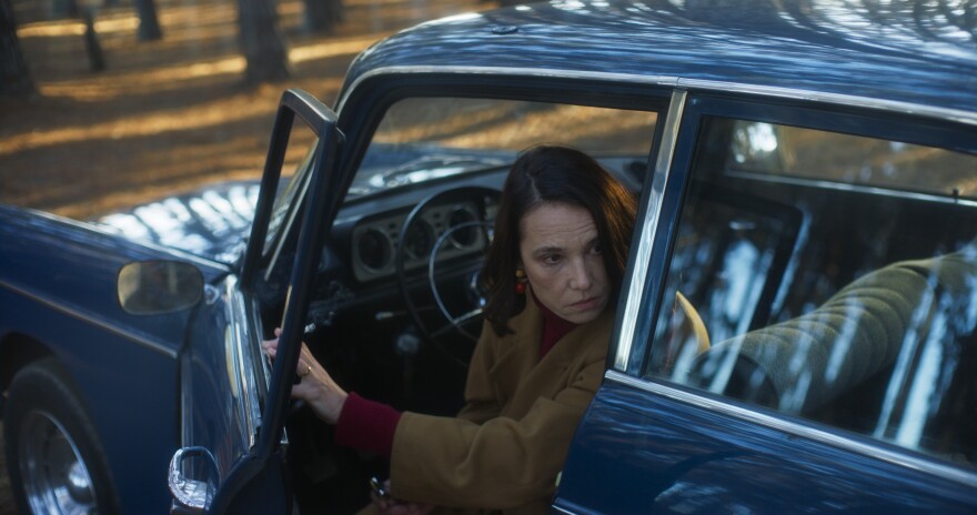  Carmen peaks out of a driver's side open car door in a blue vintage vehicle. 