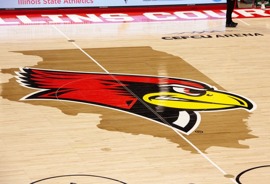 Closeup of center court in a basketball arena with a logo that features the map of Illinois with an overlay image of Illinois State's Reggie Redbird 