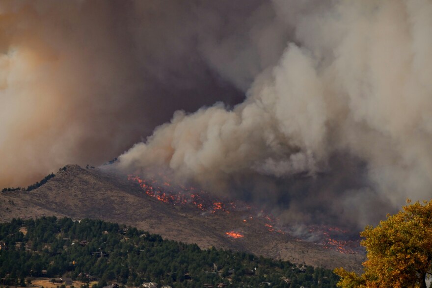 Photo of mountains with a visible wildfire across a large portion of it, smoke filling up the sky.