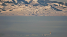 Snowy mountains with a thick inversion below them, nearly obscuring a small airport.