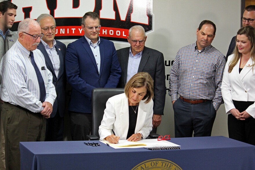 Reynolds signs the reading bill into law surrounded by state lawmakers and administrators from the ADM Community School District.