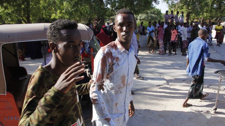 A civilian who was wounded in suicide car bomb attack is helped by a friend at checkpoint in Mogadishu, Somalia, Saturday.