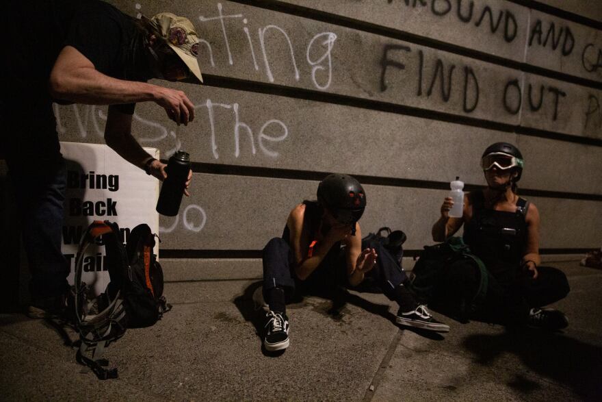 Demonstrators clean tear gas from their eyes outside the Mark O. Hatfield federal courthouse in Portland, Ore., July 25, 2020.