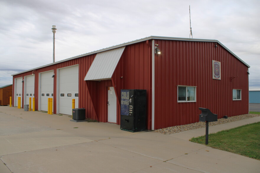A picture of the outside of a fire department in a rural area. The building is red with white doors.
