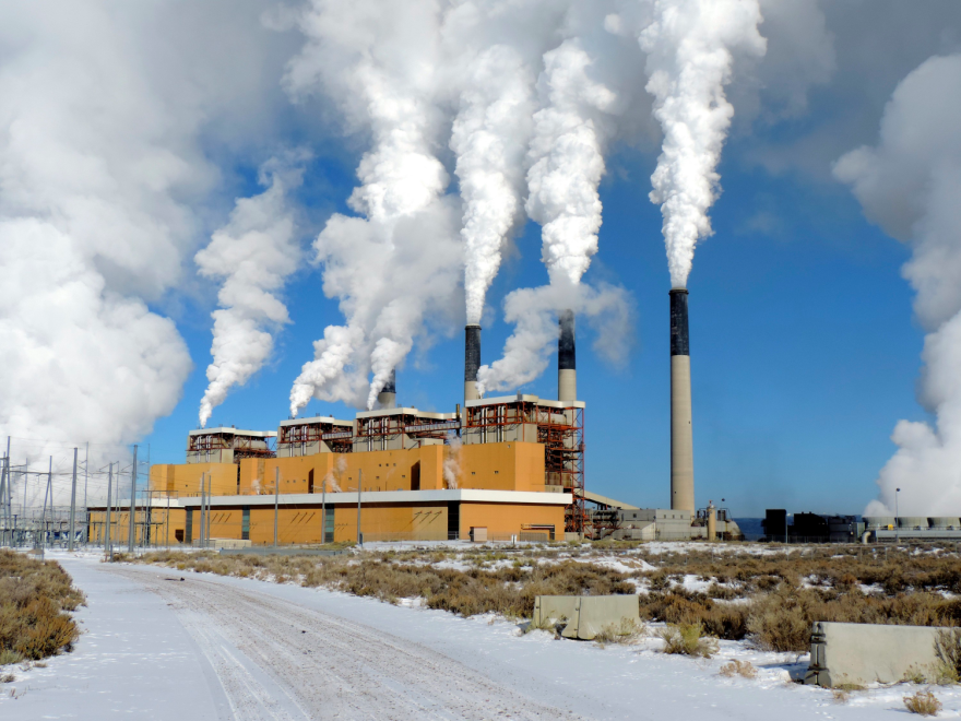 A power plant with smoke billowing out of several towering chimney stacks.