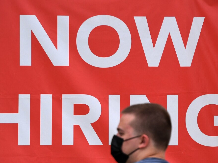 A man walks by a "Now Hiring" sign outside a store on Aug. 16  in Arlington, Virginia. Fed Chairman Jerome Powell touted the recovery of the job market in a speech on Aug. 27, but noted more progress needs to be made to return to full employment.