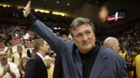 man waves to the crowd during a tribute. there are arena stands and fans in the background