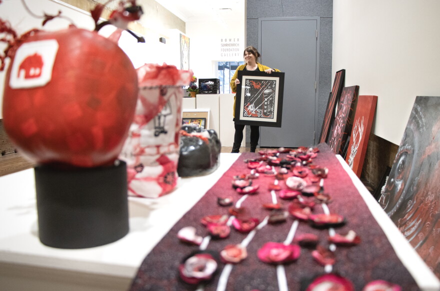 ARTSWIN Gallery Director Andrea Adams holds "Burning My Problems Away" by Lost Akuma, an entrant into the RED exhibit which opens later this month. RED was also an open call exhibit; anyone could apply.