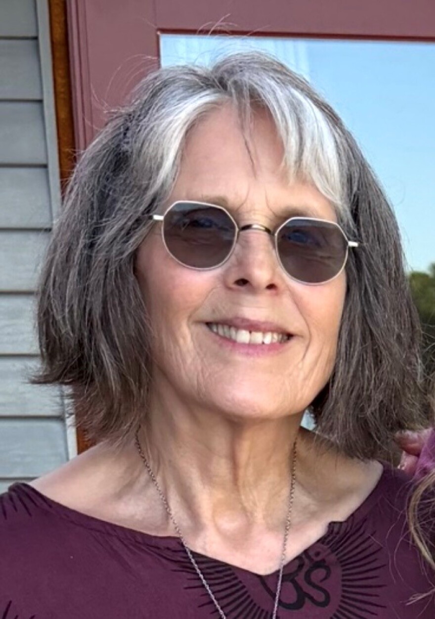 A woman wearing a purple shirt and silver necklace in front of a maroon colored door.