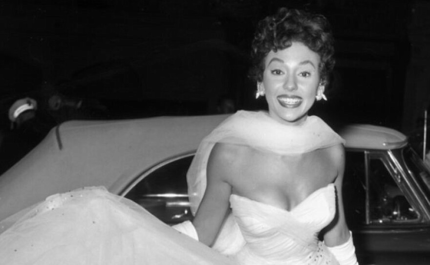 Rita Moreno smiling to the camera in a sparkly, white ballgown