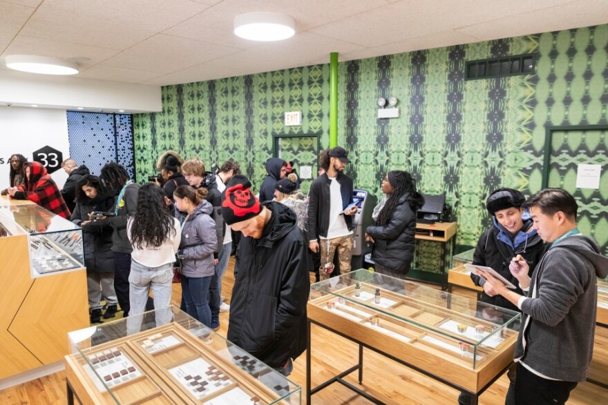 Customers crowd around tables and glass display cases showing cannabis products at a dispensary in Chicago.