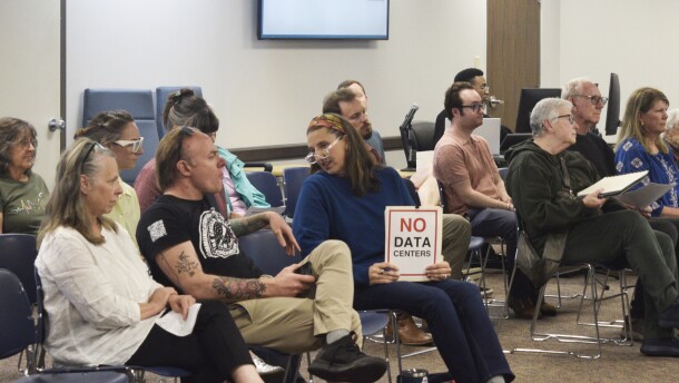 A woman holds a "No Data Centers" sign in the crowd at a city council meeting