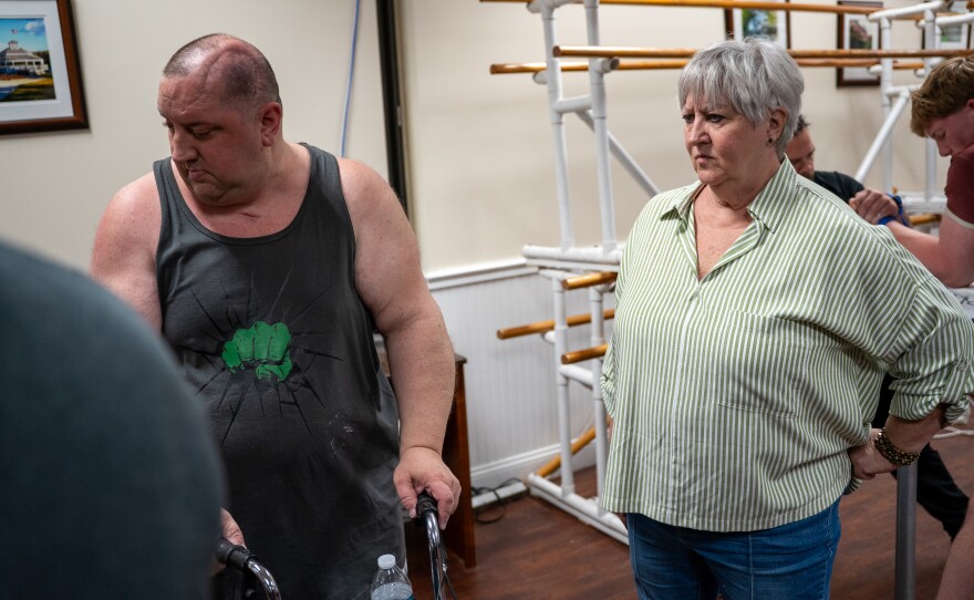Man and his mother stand in a room with others.