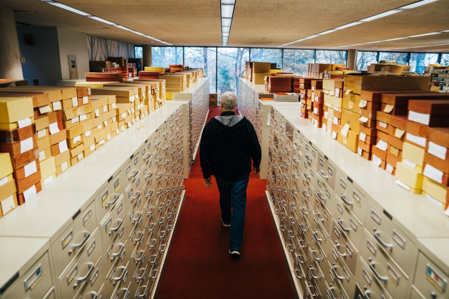 A white man walks away from many filing cabinets in a herbarium.
