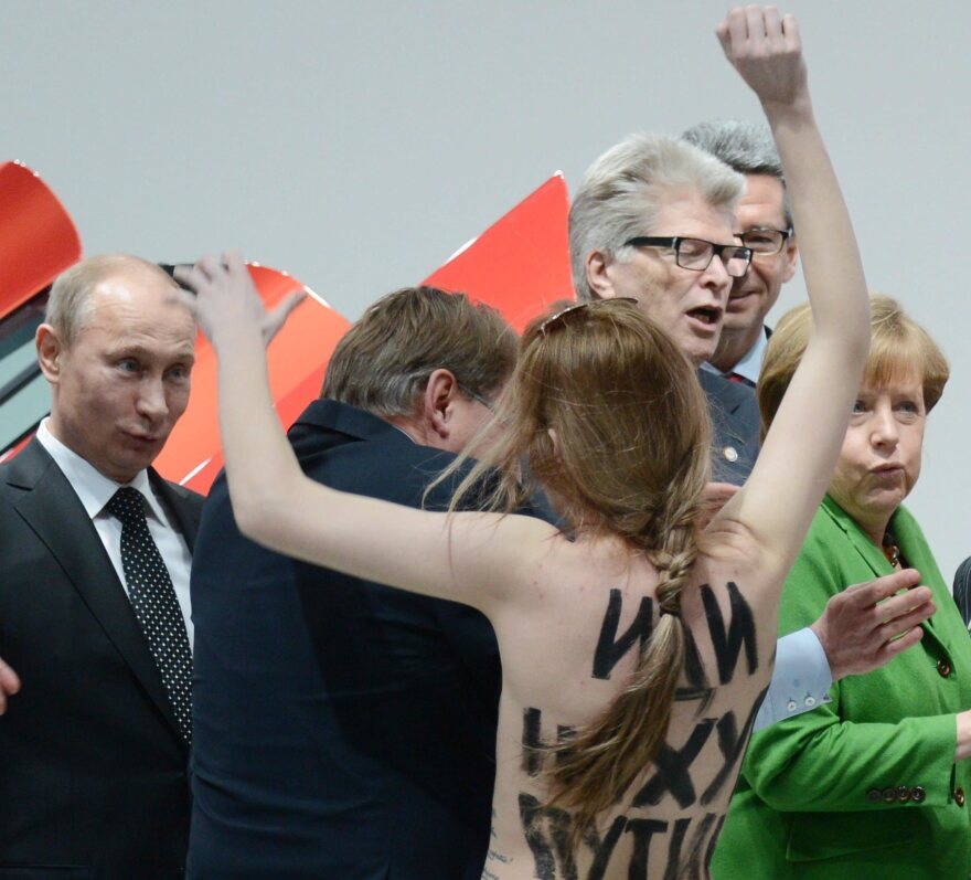 Russian President Vladimir Putin (far left) looks on Monday in Hanover, Germany, as one of three women who stripped off their tops protests his appearance at a trade fair. German Chancellor Angela Merkel is in the green jacket.