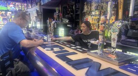 A bartender at The Blue Line is servicing a customer during lunchtime. The Bar also operates as a restaurant where customers frequent during lunch. 