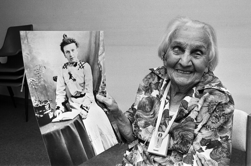 Black and white photo of centenarian Kate Willison holding a photograph of herself in her 20s.