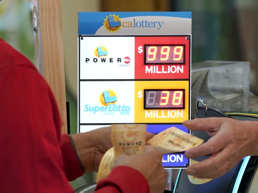 A customer is handed Powerball lottery tickets to purchased at Lichine's Liquor & Deli in Sacramento, Calif., Monday, Oct. 31, 2022. The jackpot for Monday night's drawing soared to $1.9 billion after no one matched all six numbers in Saturday night's drawing.