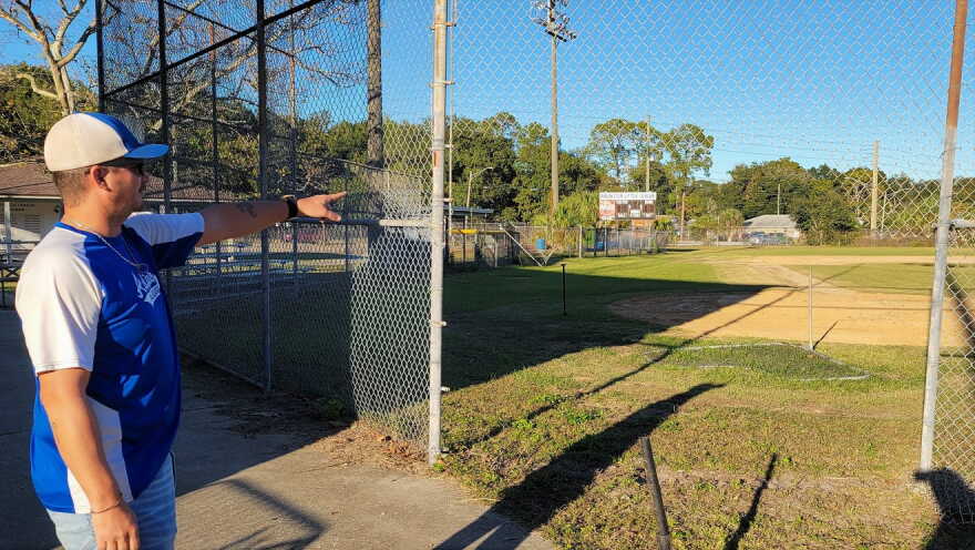 Arlington Little League Vice President Jason Rolston points to a hole in a backstop fence where thieves drove in.