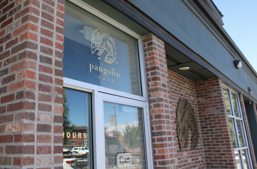 The open sign is visible behind the glass door of the front of Pangolin Cafe. An image of a pangolin is off to the right on the brick wall. 