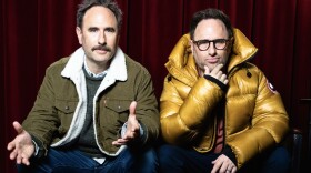 Randy and Jason Sklar sit in front of a curtain. 
