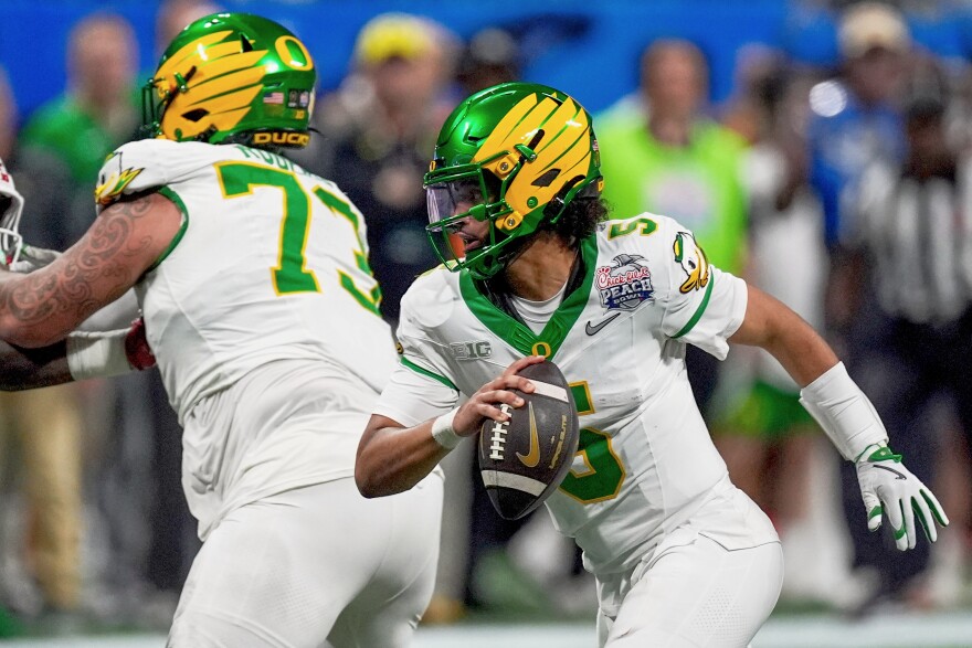 Oregon quarterback Dante Moore runs with the ball while being blocked by another Oregon player.
