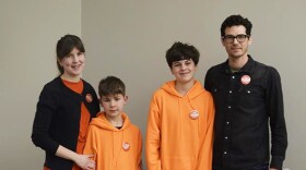 A family stands together for a photo facing the camera. Including Karen, Mitch and their two young boys. 