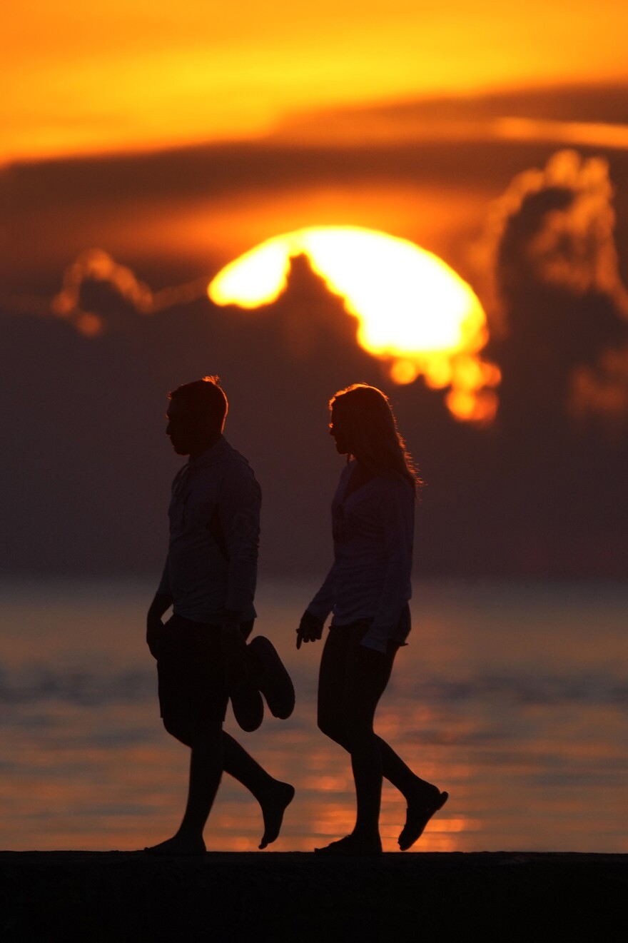 FILE - A couple walks along a jetty as the sun rises over the Atlantic Ocean, Wednesday, June 28, 2023, in Bal Harbour, Fla.