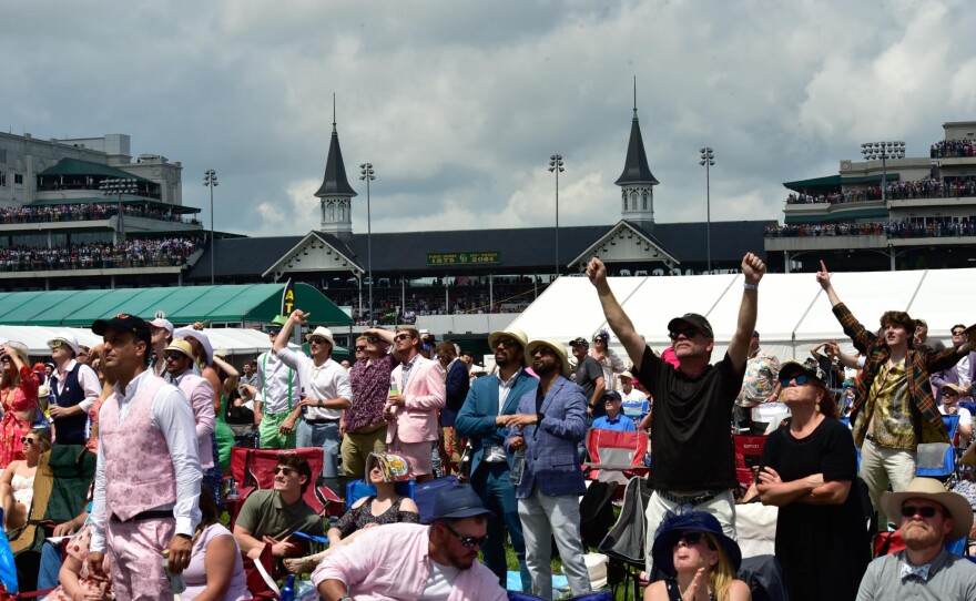 Fans in the infield of Churchill Downs watch the races from lawn chairs on a large screen.