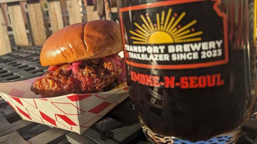A fried chicken sandwich with pickled onions, next to a bottle branded with Smoke 'n' Seoul logo.