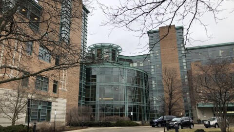 View of a circle drive in front of a multistory brick building with three-story atrium and green trim
