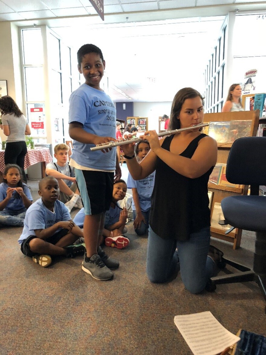 Grace Frarey, a junior at the Eastman School of Music, helping a young music-maker play the flute at an Exploration Station.