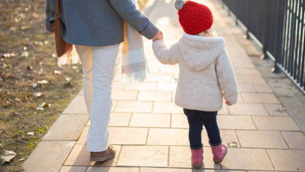 Adult and child hold hands walking down street