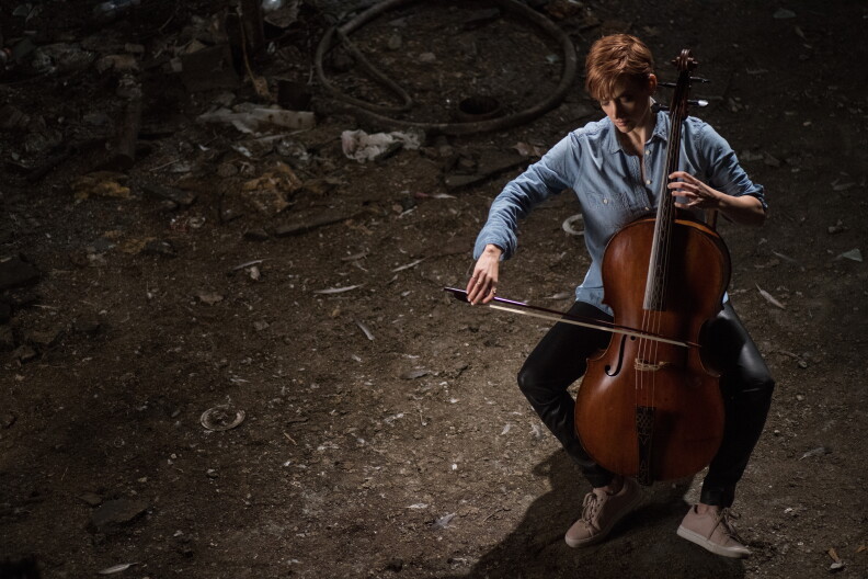 Juliana Soltis sits outside playing a cello.