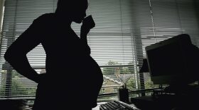 In this photo illustration, a pregnant woman is seen standing at an office desk in London, England.