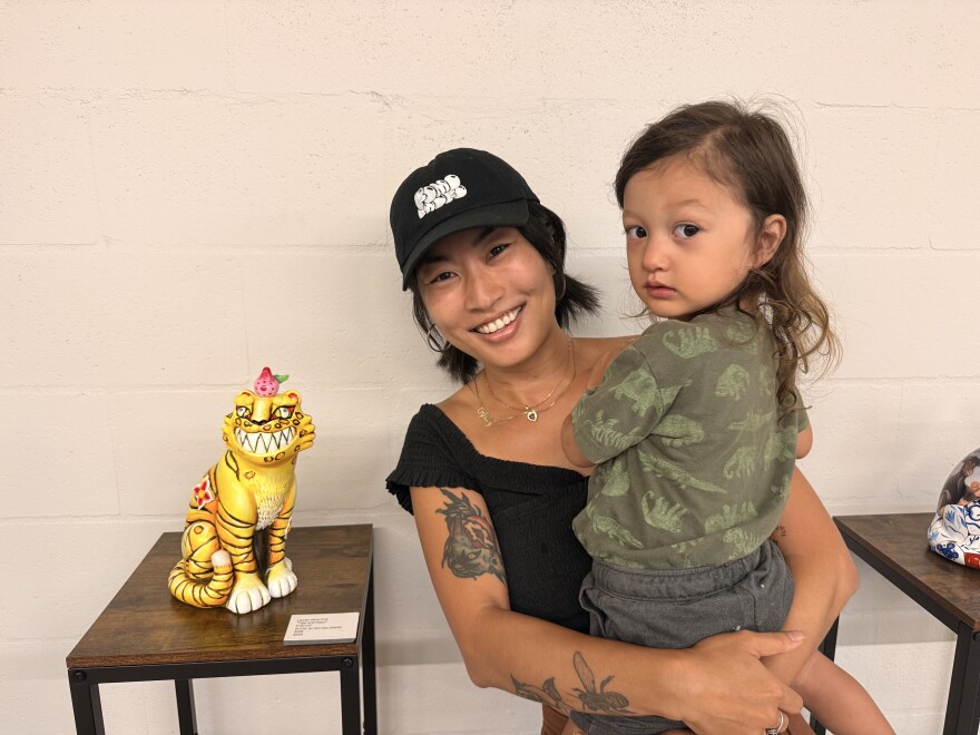 Local artist Lauren Hana Chai stands next to her work while holding her 2-year-old son, Nova.
