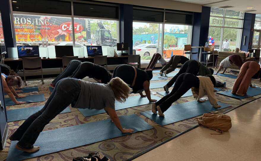 People on the ground are lined up on blue yoga mats doing yoga poses. 