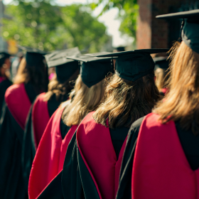 A staggered line of women in graduation robes and hats, facing away from the camera.