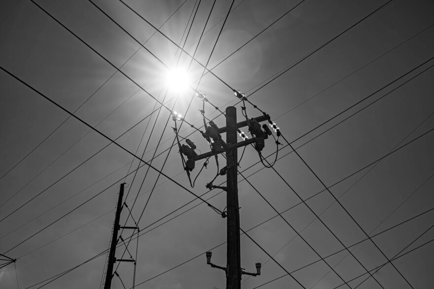 Power lines cross the sky with the sun in the background.