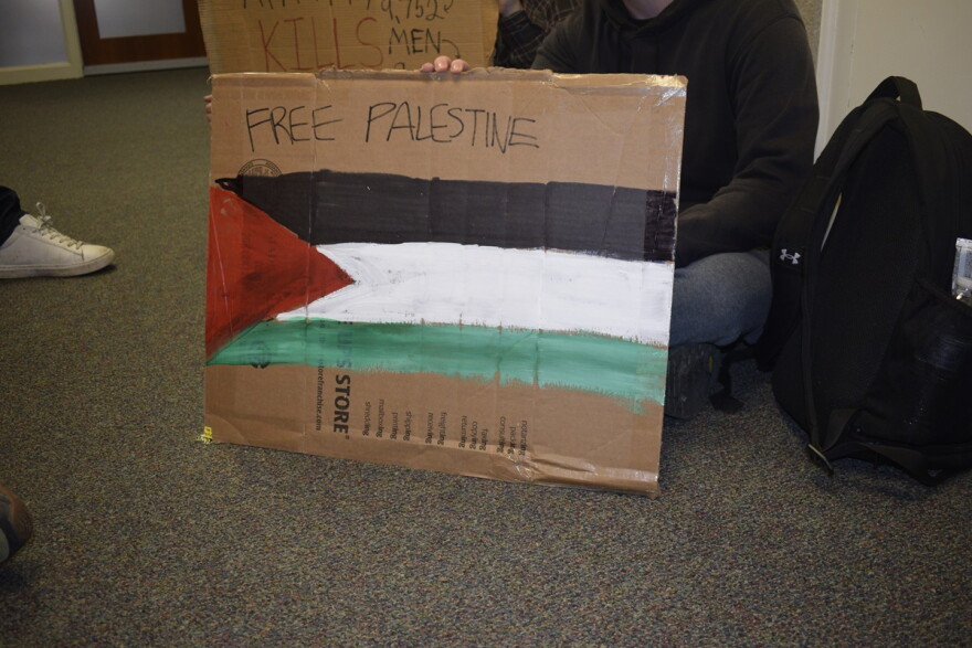 A demonstrator holds a cardboard sign that reads "Free Palestine"
