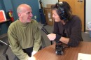 A woman holding a microphone to a man's mouth. They are seated at a table.