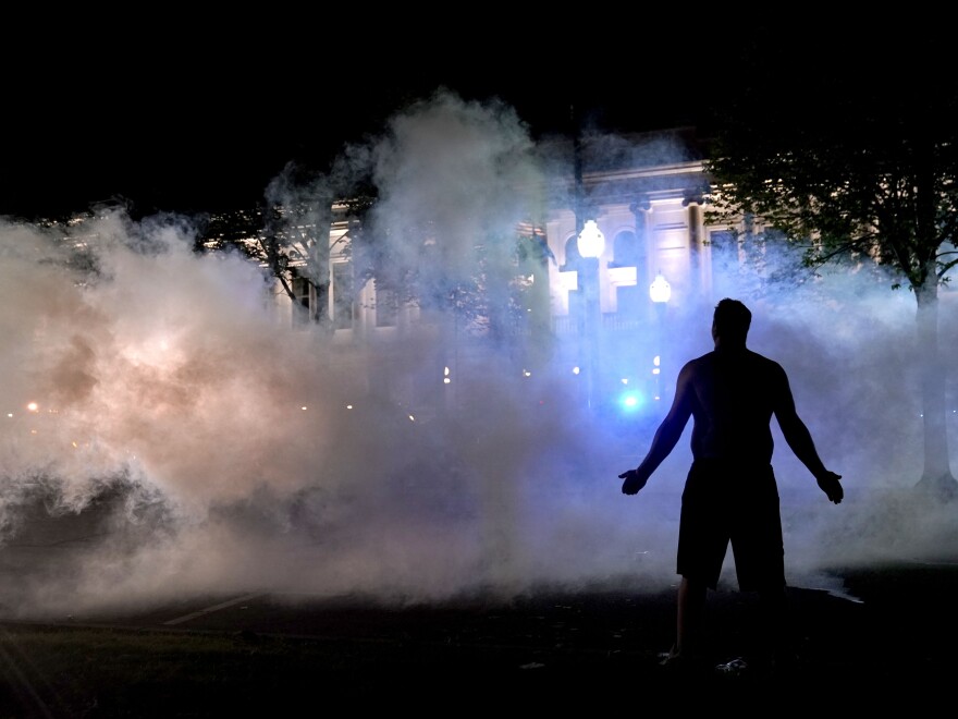 A protester attempts to continue standing through a cloud of tear gas fired by police outside the Kenosha County Courthouse late Monday.