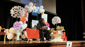 Writer on a stage expressively reads to an auditorium.