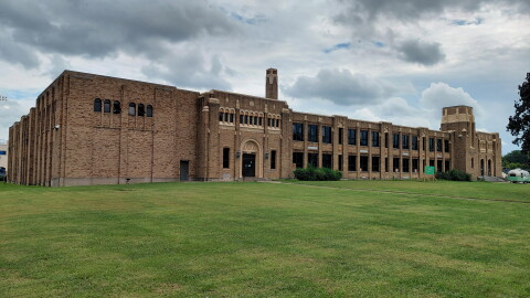 An elongated old brick school building on a slight grassy hill on an overcast day.