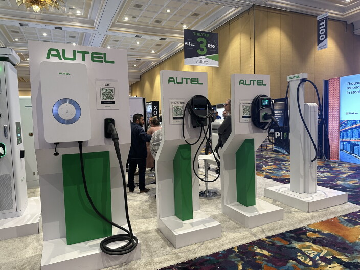A row of green-and-white charging stations are on display inside a carpeted convention center. 